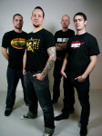 Volbeat-nelikko seisoo vaaleata taustaa vasten ryhmävalokuvassa. Miehillä on yllään mustat vaatteet, paitsi jokaisella mustissa t-paidoissaan jonkinlaisia logoja ja kuvioita.