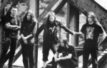 Mustavalkoinen bändikuva vuosikymmen sitten hajonneen At The Gates -yhtyeen jäsenistä, joita kuvassa viisi kappaletta. He ovat nuoria miehiä, jotka seisovat ja istuvat metallirunkoisen rakenteen edustalla.