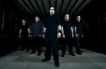 Viisi mustiin vaatteisiin pukeutunutta Mendeed-bändin jäsentä seisoo tummaseinäisessä huoneessa, jossa on tummanharmaa lattia, nuolenkärkimuodostelmassa.