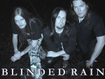 Kolme pitkähiuksista hevimiestä Blinded Rain -bändistä istuu polviensa varassa tummuutta vasten. Miehet pukeutuneet pääosin mustiin vaatteisiin, mutta vasemmassa laidassa näkyvällä hepulla jalassa metrokuvioidut maastohousut.