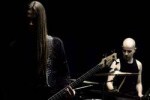 Hyvin pimeä valokuva Chthonian-bändin kahdesta miesjäsenestä, jotka seisovat täysin mustaa taustaa vasten osittain varjojen peittäminä. Etummaisena vasemmalla kitaristi tai basisti. Hänellä pitkät hiukset. Taka-alalla oikeassa laidassa kaljupäinen rumpali