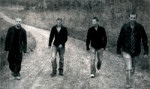 Mustavalkoinen valokuva Eventide-bändin neljästä miesjäsenestä, jotka kävelevät rivissä kapealla hiekkatiellä keskellä maaseutua. Taustalla pöpelikköä. Miehillä yllään mustaa vaatetta, osalla farkut. Heistä jokaisella lyhyet hiukset.